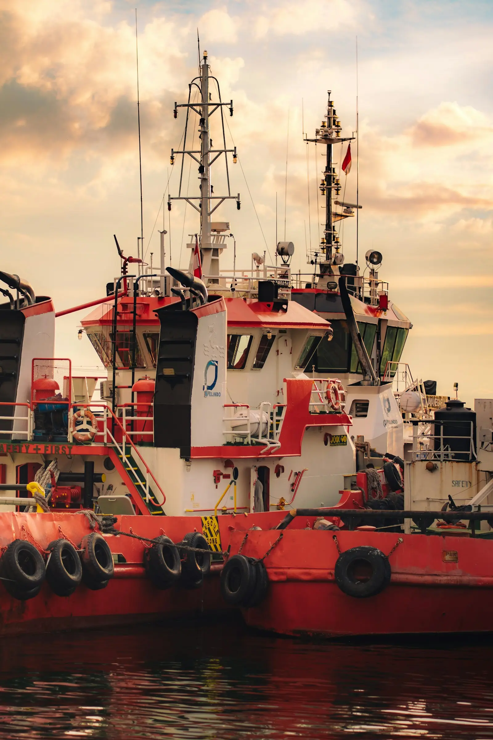 Dua kapal tunda merah bersandar di pelabuhan saat sore